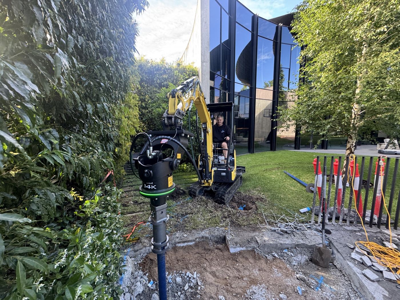 Compact excavator installing screw piles on a landscaped residential backyard
